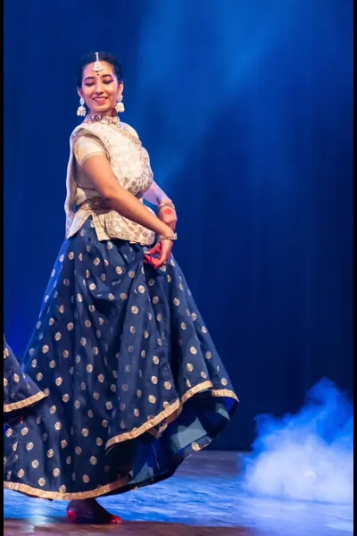 Ishita performing Kathak on stage in a blue and gold costume.