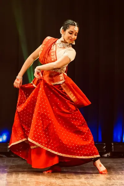 Ishita performing Kathak on stage in a red costume.