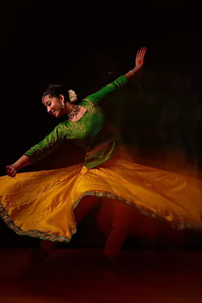 Ishita mid-spin in a yellow and green Kathak costume.